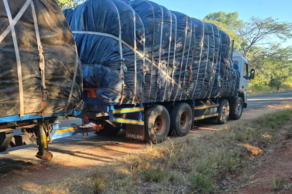 Truck and trailer carrying a large sheeted and strapped load on a road.
